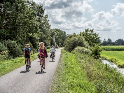 mensen die over een fietspad fietsen met daaromheen een bomen en een slootje