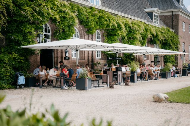Mensen genieten op het heerlijke groene terras van LIZ Restobar van hun eten en drinken en van het uitzicht op Kasteel Amerongen