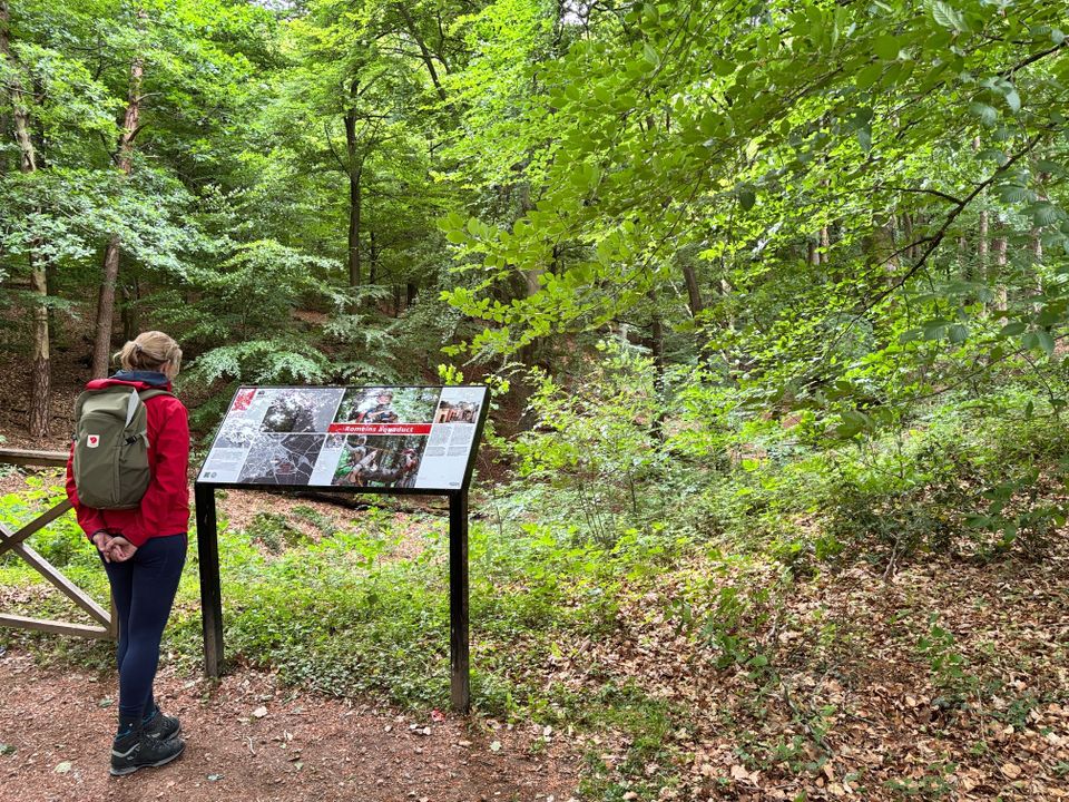 Informatiebord over de Romeinse aquaduct met wandelaarster in Orientalis, middenin het bos.