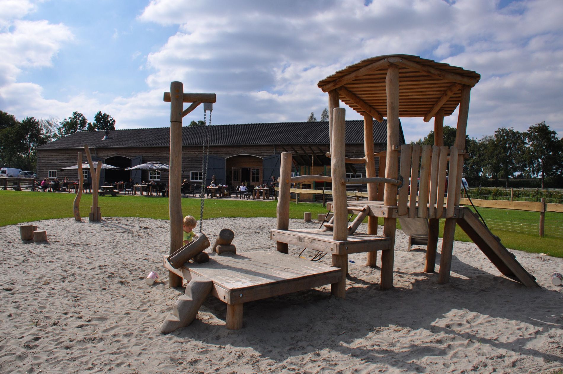 Kinderspeelplaats van De Gerrithoeve, houten klimtoestel in wit zand, omgeven door grasveld en bomen.