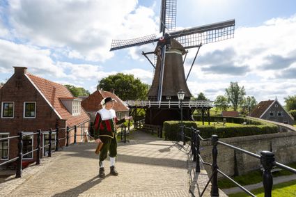 stadsomroeper op een brug in sloten met molen op de achtergrond