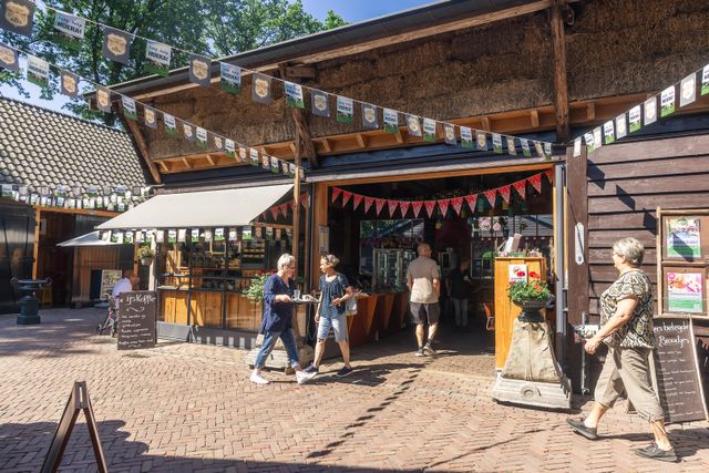 Bezoekers bij de boerderijwinkel en het terras van Hoeve Ravenstein in Baarn. De foto laat de gastvrije, landelijke sfeer van de hoeve zien, met streekproducten en horeca op het erf.
