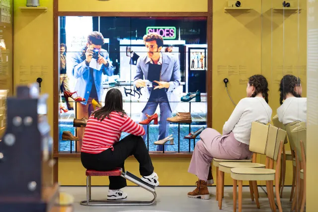 Twee bezoekers zitten op een stoel en kijken naar een video over het Schoenenkwartier