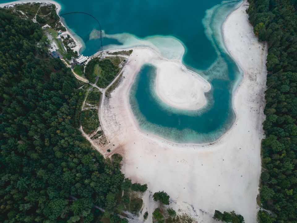 Dronefoto van een blauwe waterplas gelegen aan zand- en bosgebied in Nederland