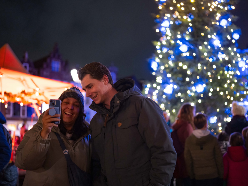 een man en een dame die samen een selfie maken met de kerstboom in Delft