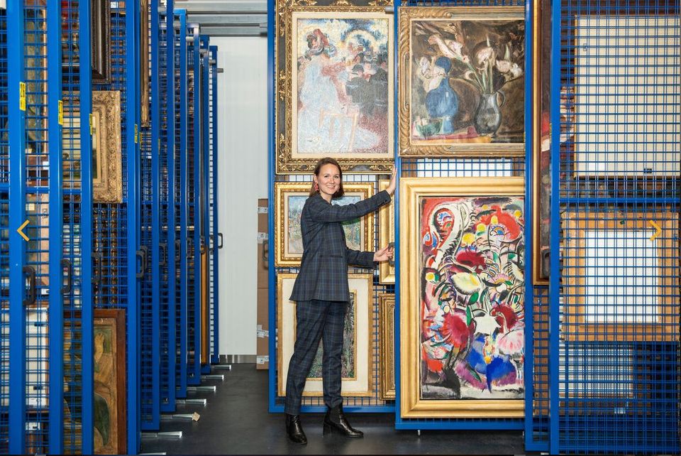 Conservator laat in het depot van Singer Laren kunstwerken op een wand zien, door deze uit het rek te trekken.