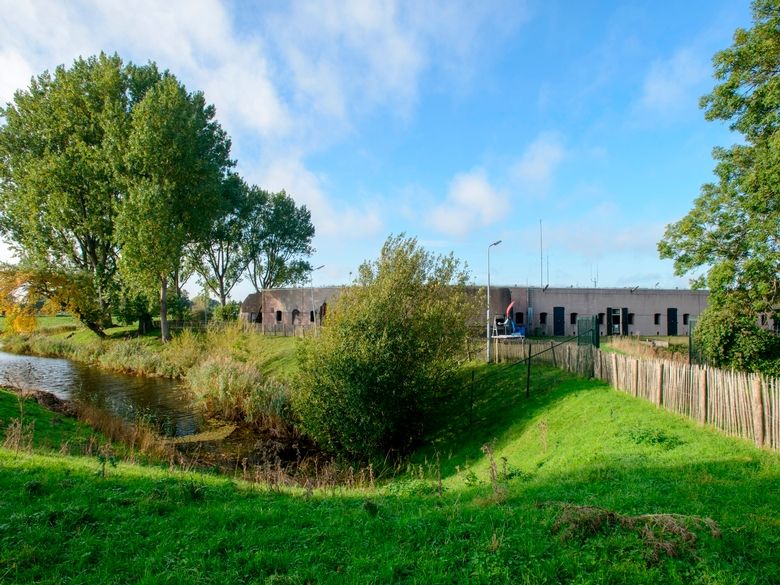 Een betonnen fort achter een houten hek, in het gras.