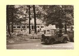 Oude zwart-wit foto van Groot Speijck met terras met witte stoeltjes en tafeltjes in een bosrijke omgeving. Op de voorgrond staat een oude locomotief met een open wagon erachter.