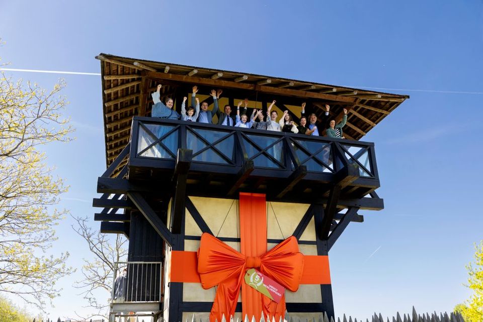 Op de galerij van de Romeinse wachttoren staan mensen, de wachtoren heeft een grote oranje strik met 5 jaar werelderfgoed erop.
