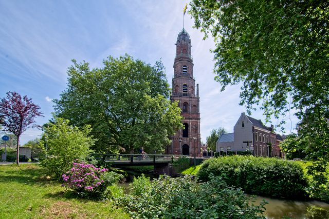 Fietser steekt het bruggetje over bij de Oude Nicolaaskerk in IJsselstein, omringd door groen en water, midden in het Groene Hart van Holland.