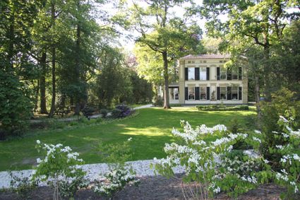 Historische buitenplaats in Woerden, provincie Utrecht, Groene Hart, statig herenhuis omringd door een groene parkachtige tuin met oude bomen, gazon en bloeiende struiken.