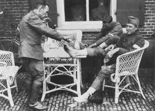 Drie Nederlandse militairen helpen elkaar met hun voetverzorging tijdens een rust in de 20e Vierdaagse