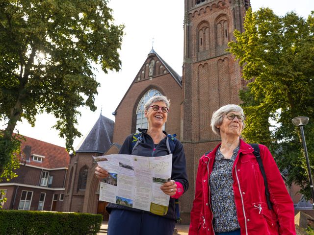 Twee wandelaars die naar een routekaart kijken voor een kerk.
