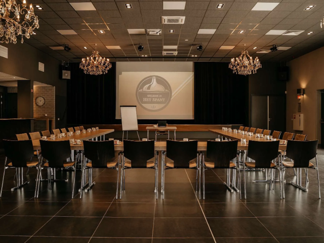 De zaal van Het Spant Ameide, er staan rijen met stoelen en een groot beamerscherm.