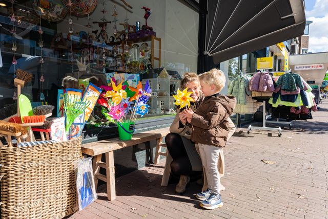 Een moeder en haar zoon staan bij een winkel die aan het kijken zijn bij kleurrijke windmolentjes