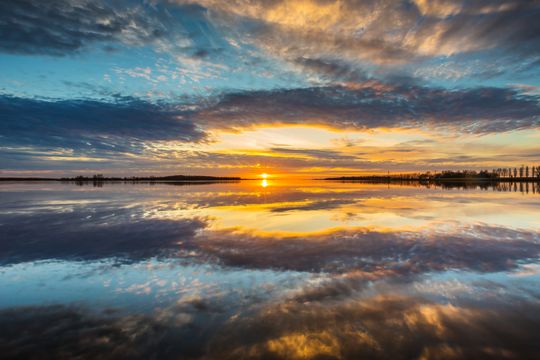 Prachtige weerspiegeling van de kleuren van de ondergaande zon op het water bij de Ramspolkering in de Noordoostpolder.