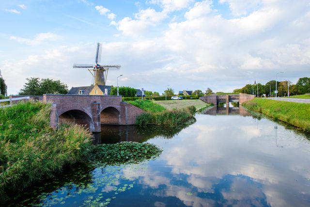 Een bakstenen sluis met verschillende onderdoorgangen voor het water. Op de achtergrond zie je een oude molen.