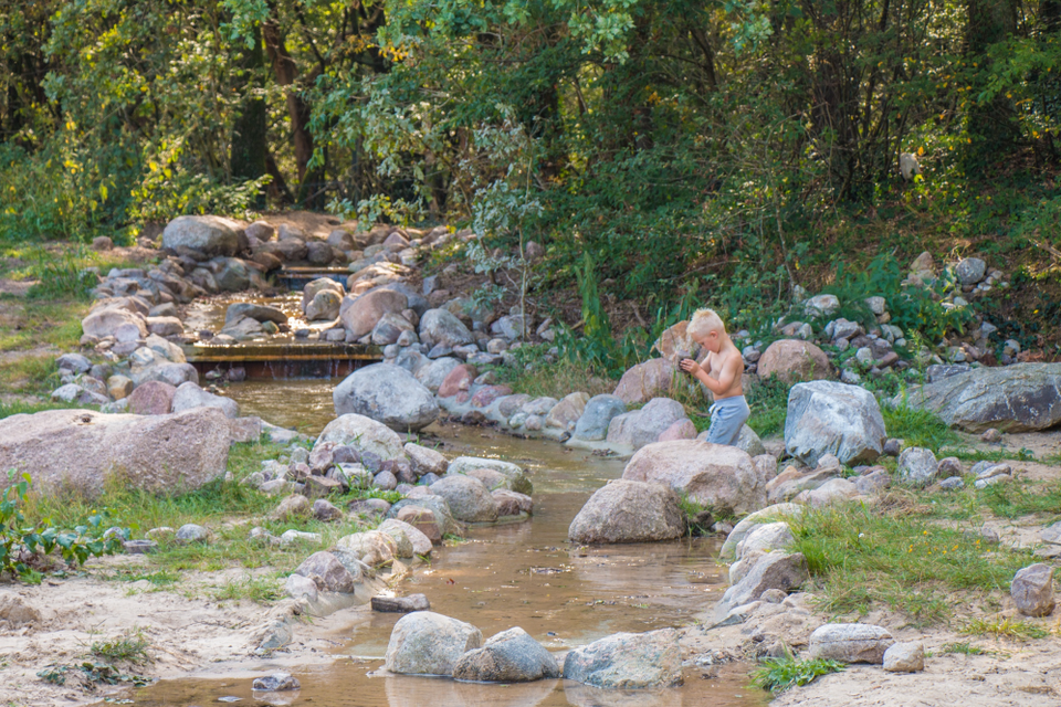 Een jongetje speelt bij een stroompje water met zand en keien.