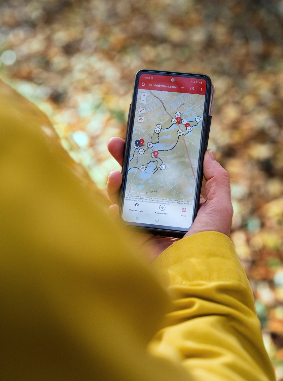 Een hand met daarin een telefoon waarop een route zichtbaar is.