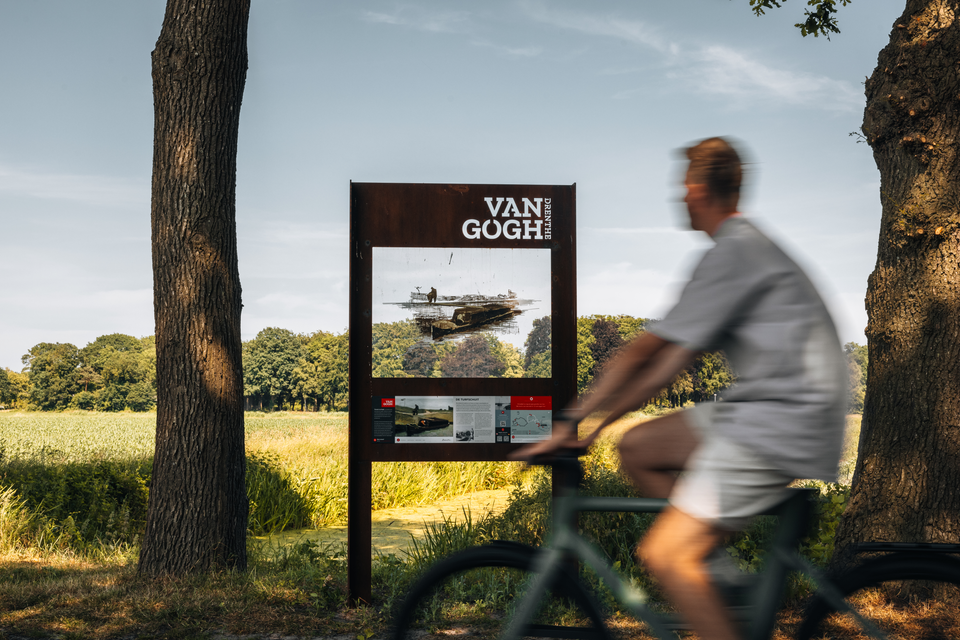 Een man fiets langs een doorkijkpaneel en ziet waar Van Gogh het schilderij De Turfschuit creëerde.