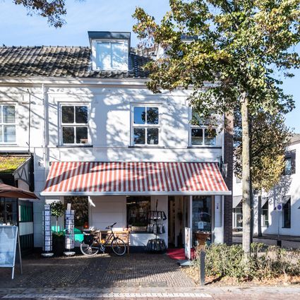 Witte gevel met afdak en boom aan de rechterkant.