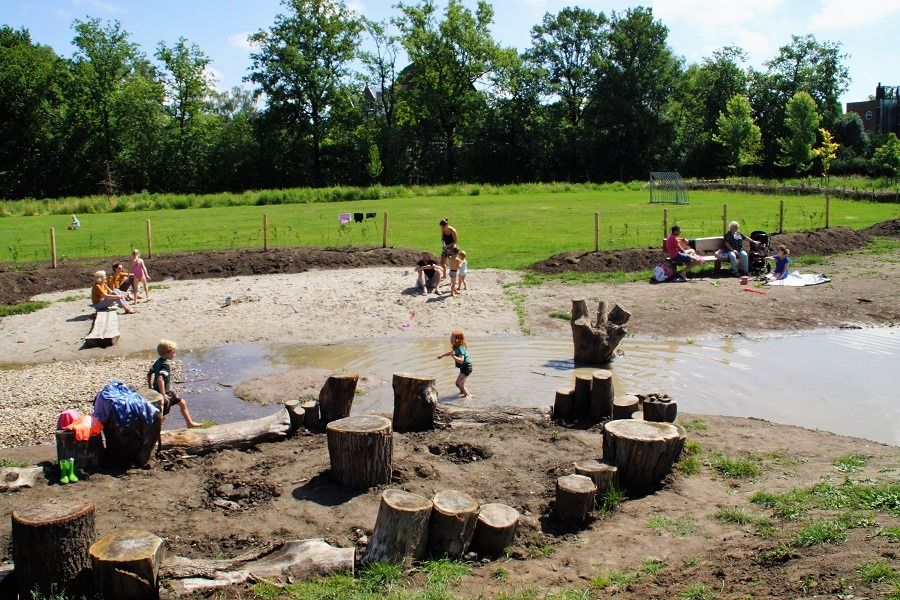 Kinderen spelen bij water en boomstammen in de speelweide van Landgoed Bredius in Woerden.