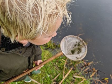 Een jongetje met een schepnet van bovenaf gefotografeerd.