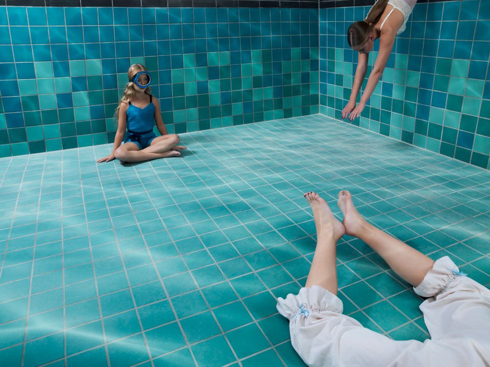 Kinderen zitten op bodem van blauw betegeld zwembad