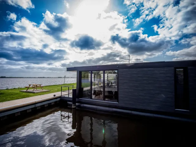 Vakantiewoonboot De Waterparel in Offingawier van de zijkant met een indrukwekkende wolkenlucht aan de hemel.