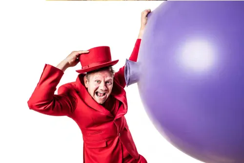 De ballonnenman in een rood pak naast een super grote paarse ballon