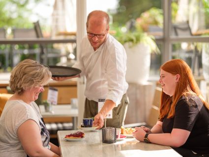 Een man seveert koffie aan een tafel met twee vrouwen.
