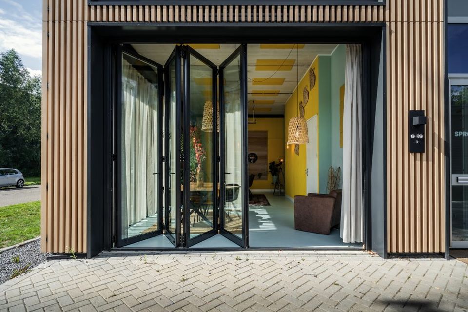 Een foto van de voorgevel met de deuren geopend, je kunt de gekleurde ruimte deels inkijken.