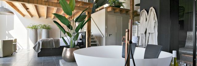 Slaapkamer met 2-persoons bed onder een vide, luxe inrichting. Op de voorgrond staat een vrijstaand wit bad en er hangen badjassen.