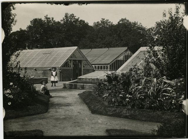 Een jongen en een meisje bij de kassen voor bloemen en vruchten van de Gerard Adriaan van Swieten Tuinbouwschool in Frederiksoord. Deze foto verscheen in het jaarboekje van oud-leerlingen van de school voor 1905, uitgegeven in 1904.