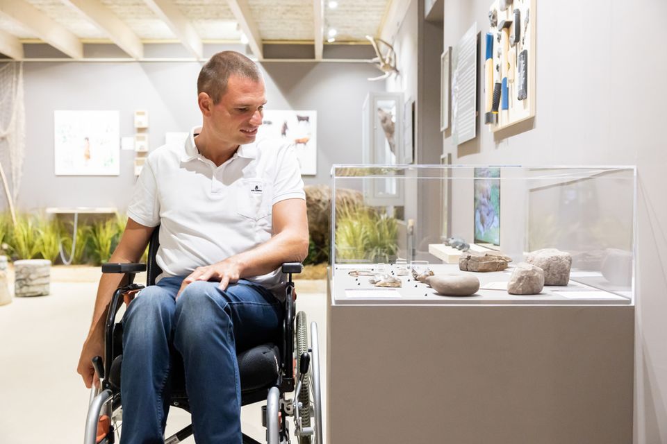 Een man in een rolstoel kijkt naar een tentoonstelling in een museum.