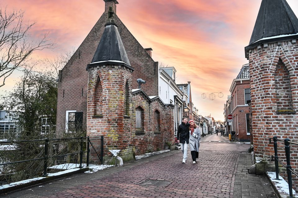 Stel wandelt door de oude binnenstad van IJsselstein op een winterse dag, met een kleurrijke zonsondergang en historische gebouwen in het Groene Hart.