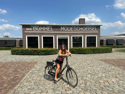 Chloe Sterk van Daily Nonsense staat met haar fietst voor het hoofdgebouw van Schoenfabriek Van Bommel in Moergestel