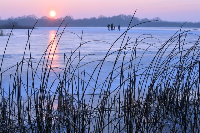 Schaatsers op natuurijs op de Ankeveense Plassen bij een ondergaande zon