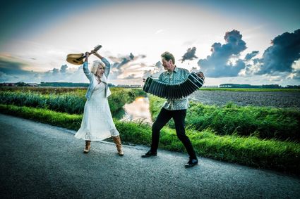 Leoni Jansen staan met haar gitaar links en Carel Kraayenhof met zijn bandoneon rechts op een landweg in een polder landschap.