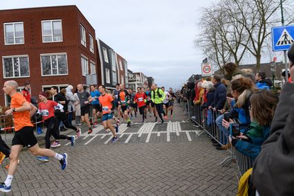 Groep hardlopers tijdens de Linschotenloop door de straten van Linschoten met langs de hekken supporters die kijken en aanmoedigen.