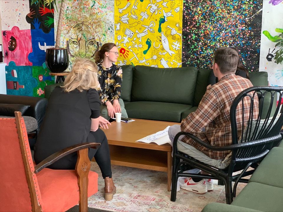 3 vrouwen en jongen rondom een tafel in gesprek met kleurrijke achtergrond