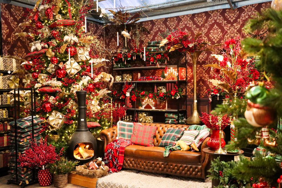 Kerstshow bij Tuincentrum De Bosrand in Woerden, provincie Utrecht, met een rijk versierde kerstboom, sfeervolle kerstverlichting, rode en gouden kerstdecoraties, een leren bank en een houtkachel.