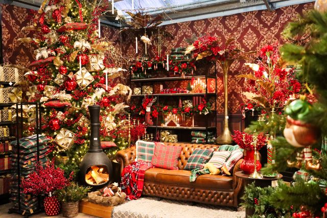 Kerstshow bij Tuincentrum De Bosrand in Woerden, provincie Utrecht, met een rijk versierde kerstboom, sfeervolle kerstverlichting, rode en gouden kerstdecoraties, een leren bank en een houtkachel.