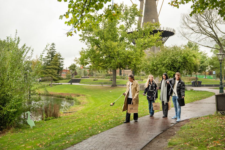 Campagnebeeld van Let's Bloomit, Love Leiden. Vier personen wandelen en gapen afval met grijpers in het Singelpark.