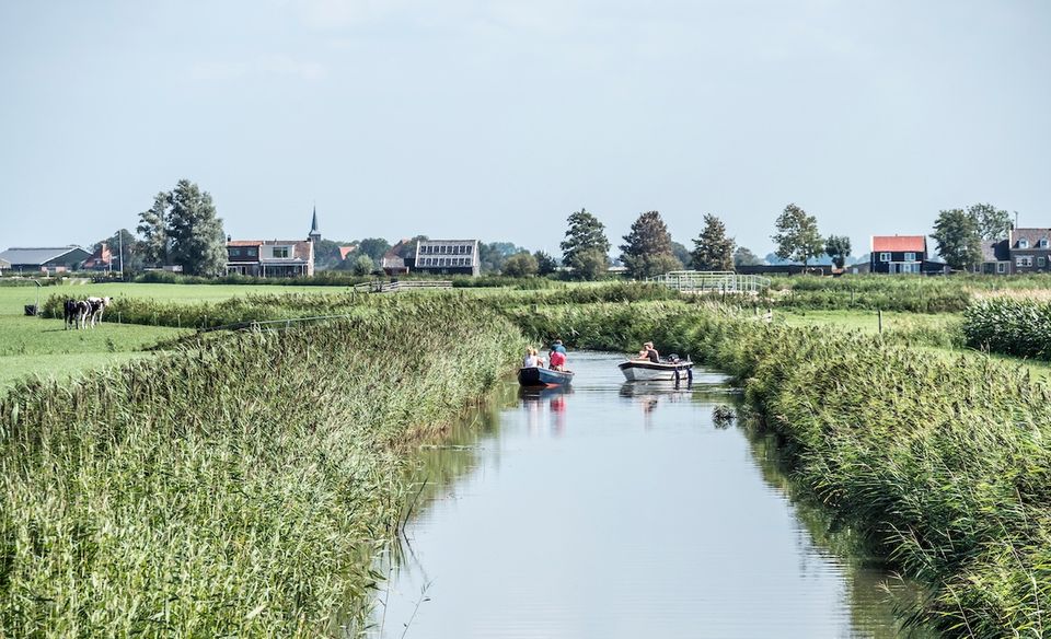 twee bootjes die in de sloot varen tussen de weilanden