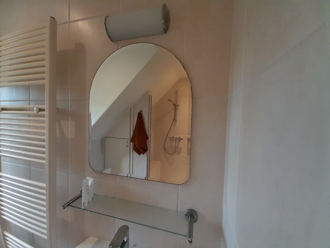 Detailfoto van een witte badkamer, met spiegel waarin de inloopdouche weerspiegelt wordt en een witte handdoekradiator.
