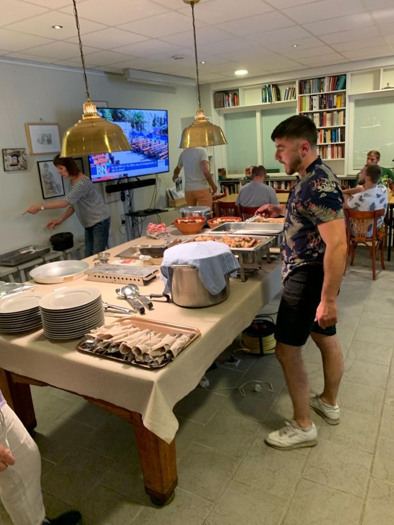 Mensen staan en zitten rond een tafel met diverse gerechten.