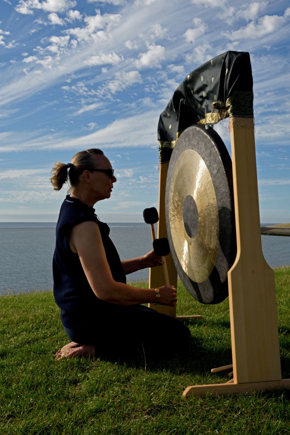 Vrouw bespeelt gong op dijk