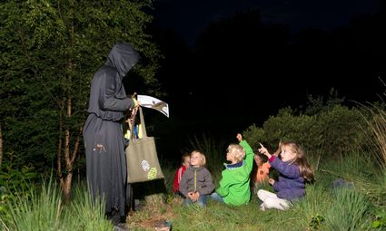 Groep kinderen die onder leiding van gids in het donker het bos ontdekken