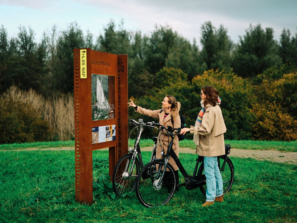 Twee jonge vrouwen staan met hun fietsen bij een Toeristisch OverstapPunt een route uit te zoeken